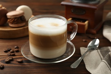 Aromatic coffee in cup, beans, spoon and macarons on wooden table