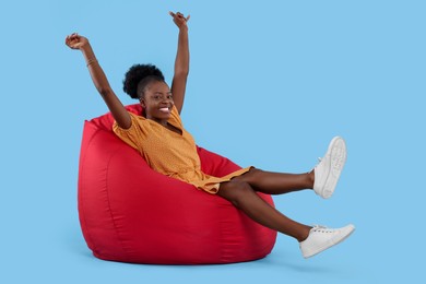 Beautiful young woman sitting on beanbag chair against light blue background