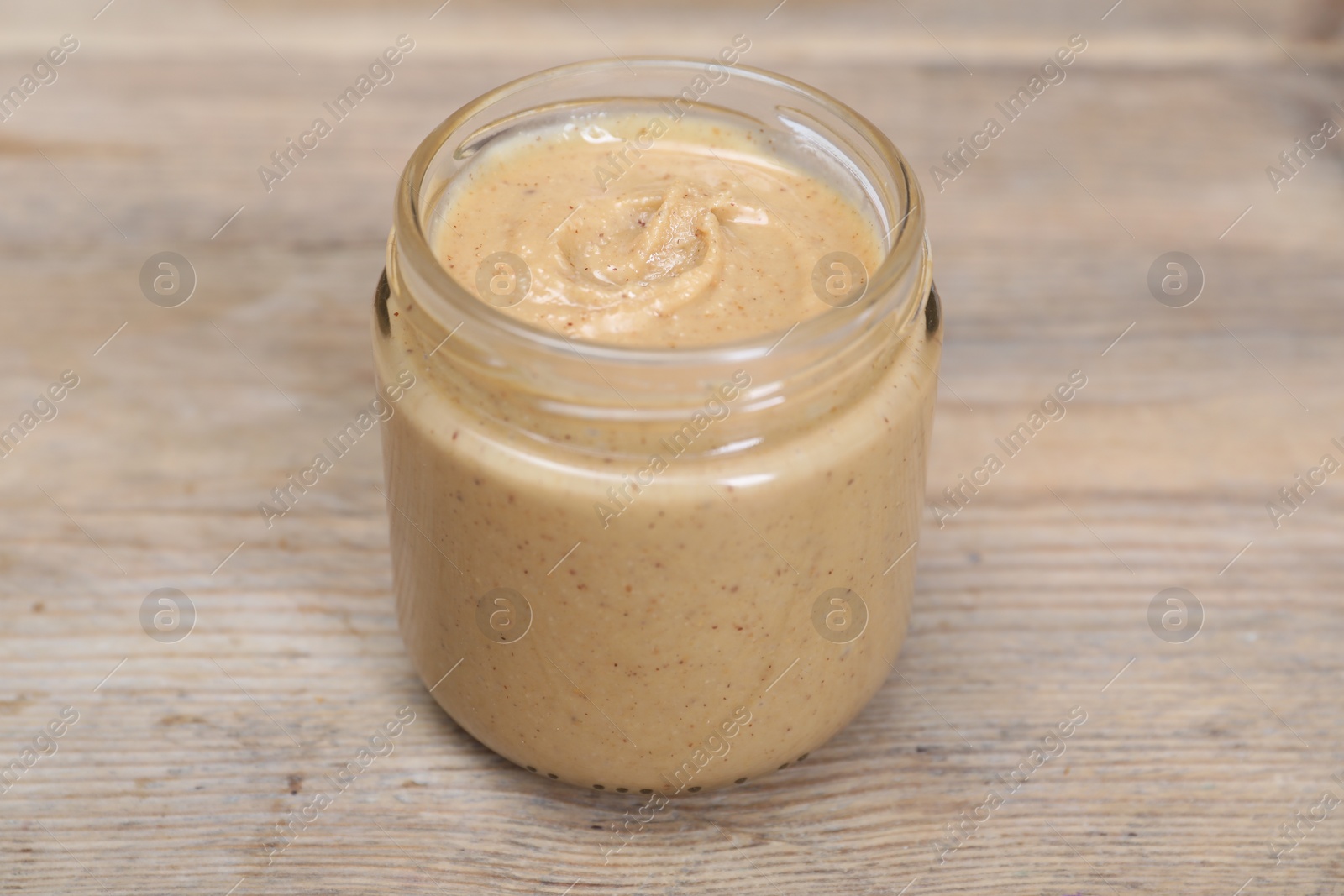 Photo of Tasty nut paste in jar on wooden table, closeup