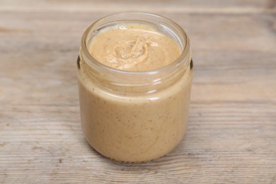 Tasty nut paste in jar on wooden table, closeup