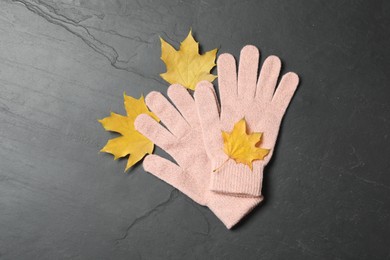 Photo of Stylish pink woolen gloves and dry leaves on black table, flat lay