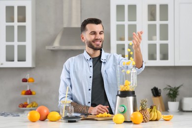 Photo of Handsome man adding mango into blender with ingredients for smoothie in kitchen