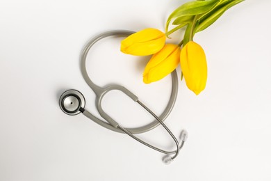 Photo of Stethoscope and yellow tulips on white background, flat lay. Happy Doctor's Day