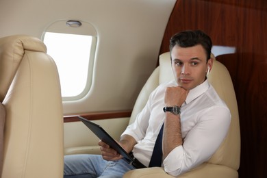 Photo of Businessman with earbuds working on tablet in airplane during flight