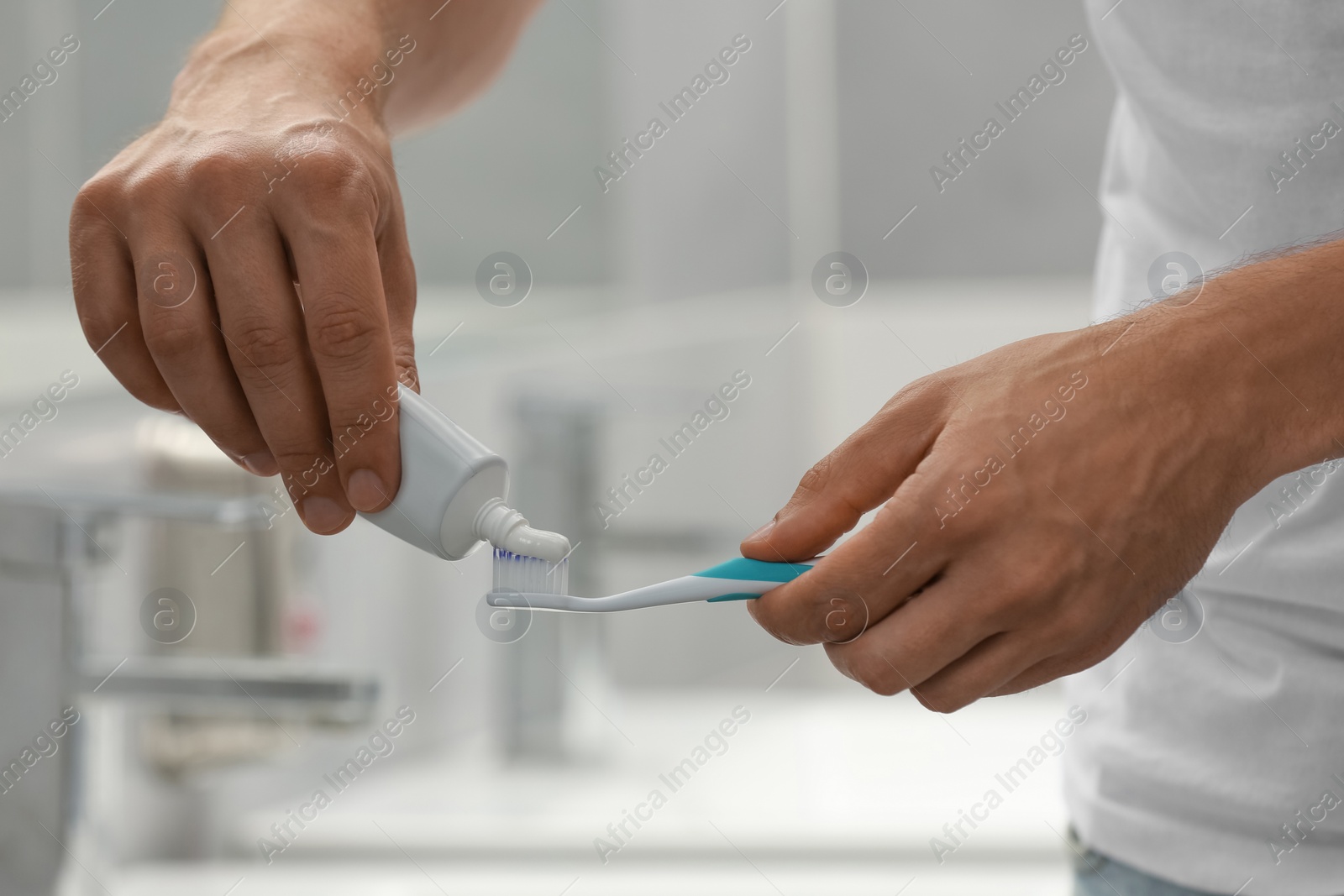 Photo of Man applying toothpaste on brush in bathroom, closeup