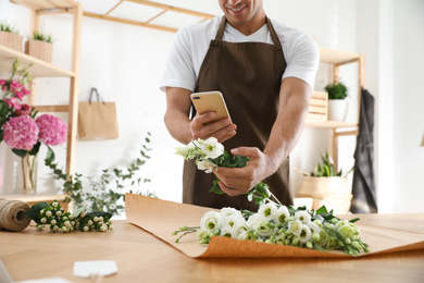 Photo of Florist taking picture of beautiful flowers in workshop, closeup