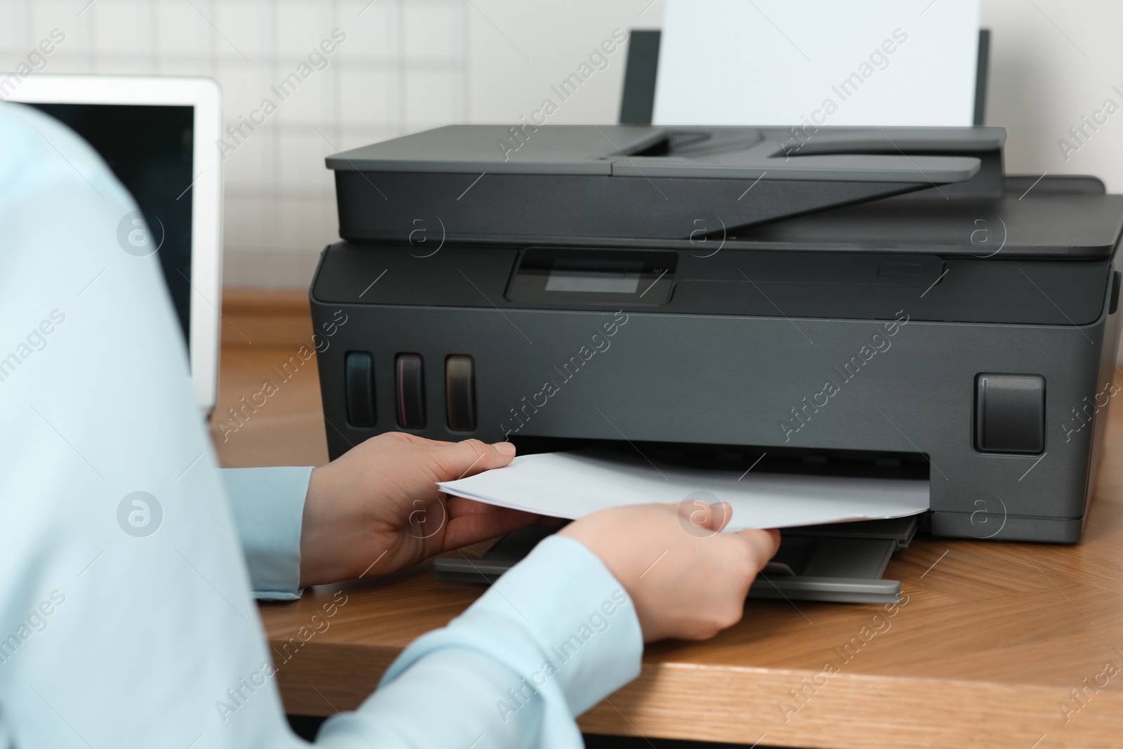 Photo of Woman loading paper into printer at wooden table indoors, closeup