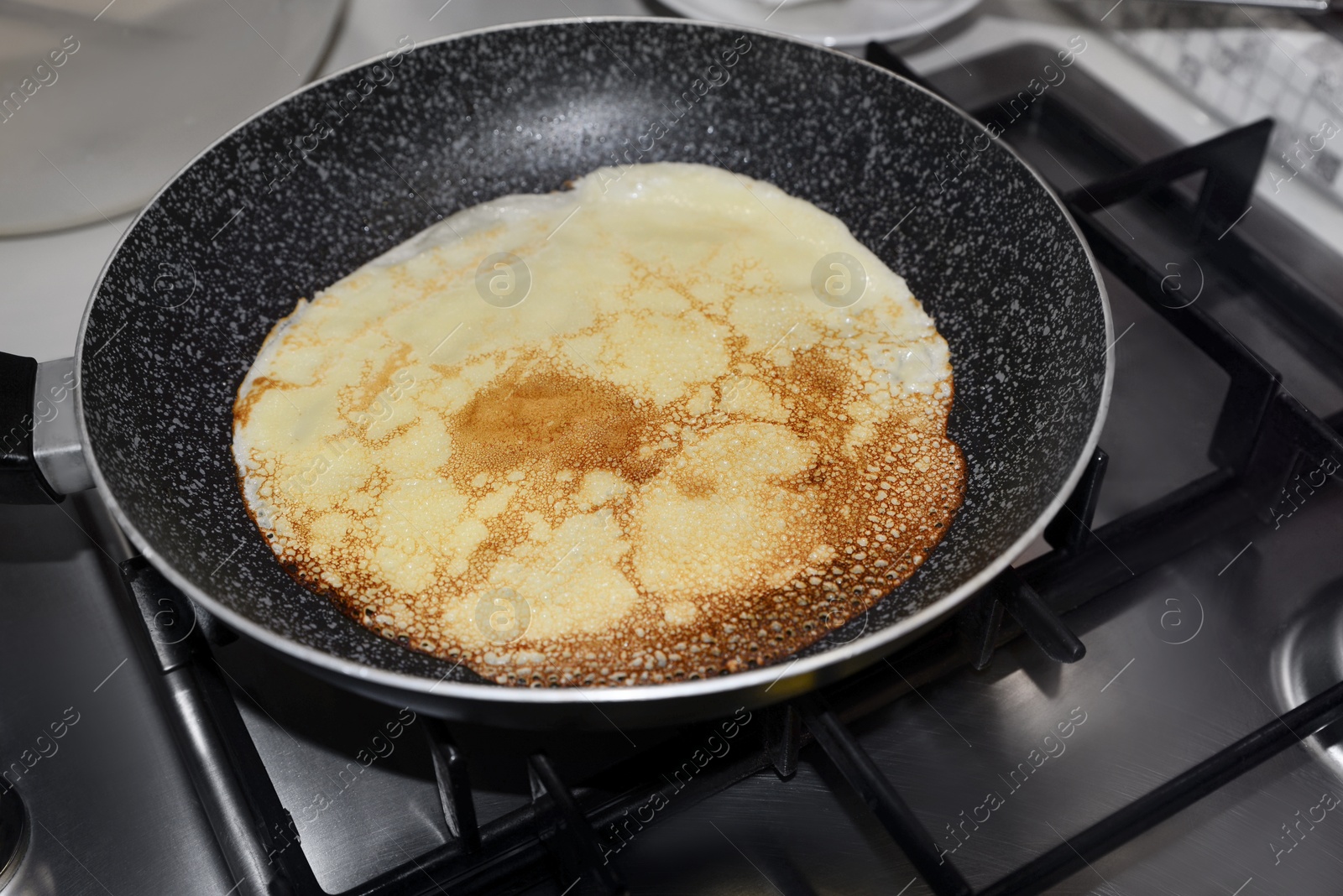 Photo of Frying delicious crepe on pan in kitchen, closeup