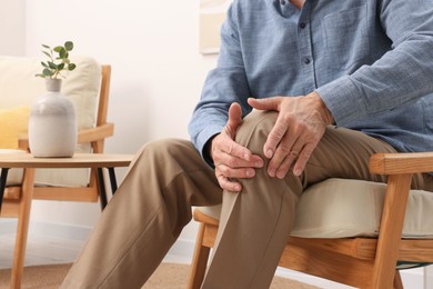 Senior man suffering from pain in his knee at home, closeup. Arthritis symptoms