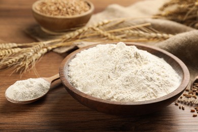 Bowl and spoon with flour on wooden table