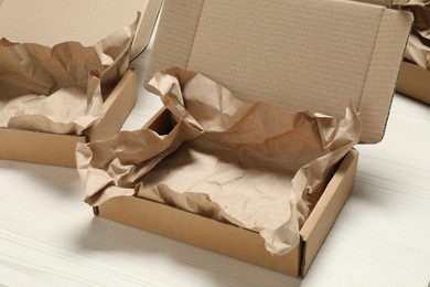 Photo of Open cardboard boxes with crumpled paper on white wooden floor