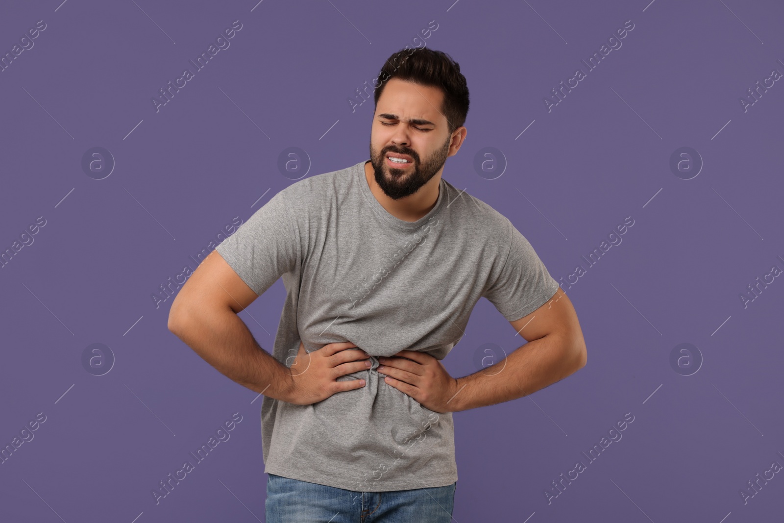 Photo of Young man suffering from stomach pain on purple background