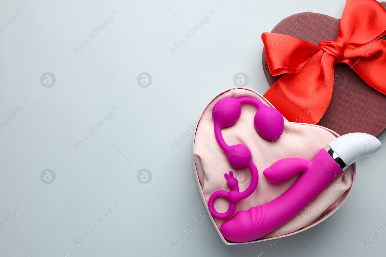 Photo of Pink sex toys in heart shaped gift box on white background, flat lay. Space for text