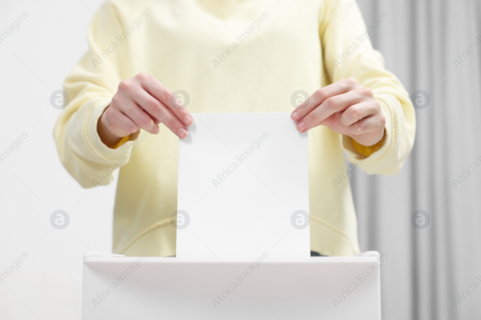 Photo of Woman putting her vote into ballot box on blurred background, closeup