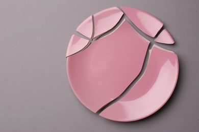 Pieces of broken pink ceramic plate on grey background, top view. Space for text