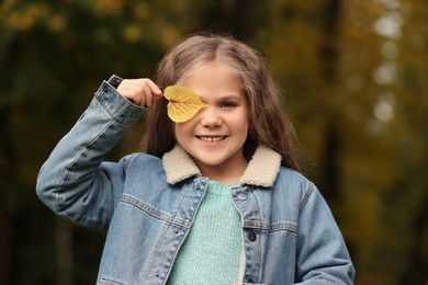 Portrait of happy girl covering face with autumn dry leaf outdoors