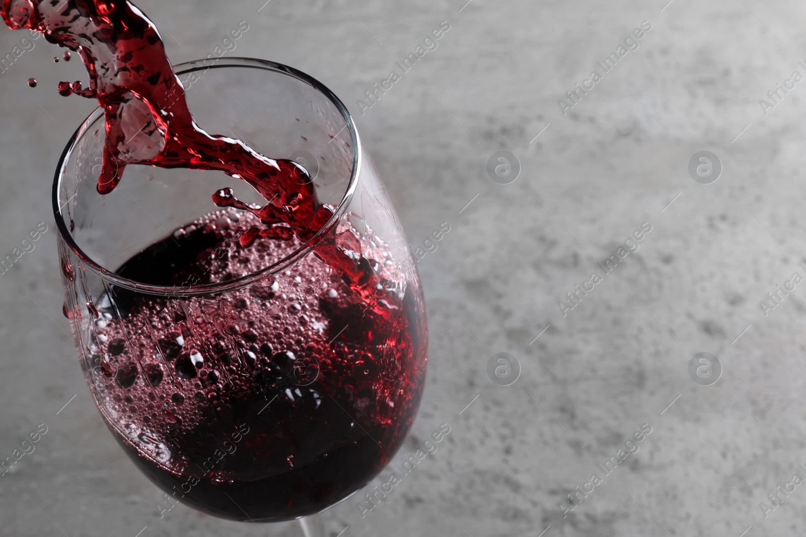 Photo of Pouring tasty red wine in glass at gray table, closeup. Space for text