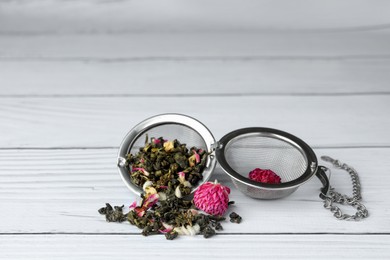 Photo of Snap infuser with dried herbal tea leaves and flowers on white wooden table. Space for text
