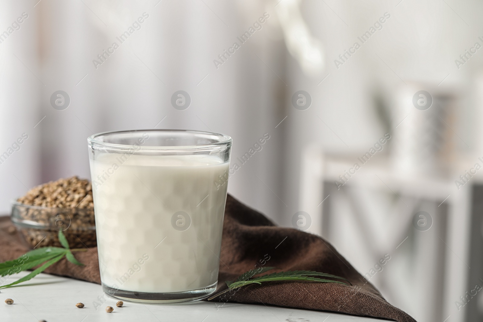 Photo of Glass of hemp milk on white table against blurred background