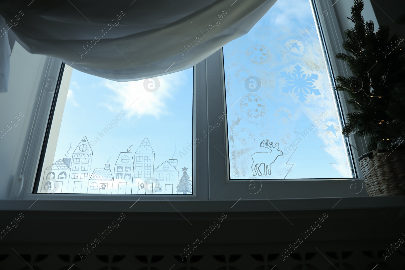 Photo of Beautiful drawing made with artificial snow on window at home, low angle view. Christmas decor