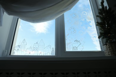 Photo of Beautiful drawing made with artificial snow on window at home, low angle view. Christmas decor