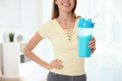 Photo of Young woman with bottle of protein shake at home, closeup