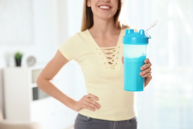 Young woman with bottle of protein shake at home, closeup