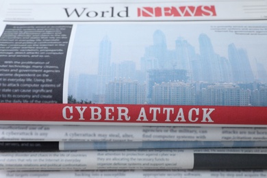 Photo of Stacked newspapers with headline CYBER ATTACK as background, closeup