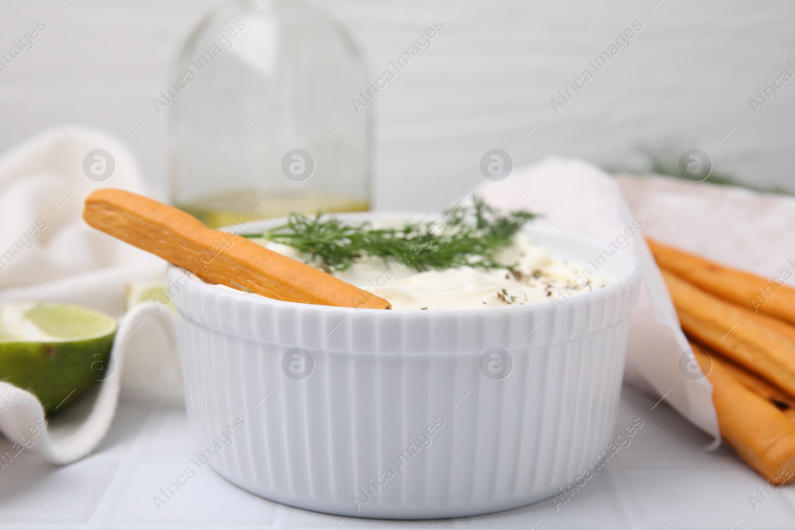 Photo of Delicious cream cheese with grissini stick and dill on white tiled table, closeup