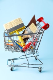 Photo of Different construction tools in shopping cart on light blue background