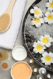 Bowl of water with flowers and different spa supplies on light grey table, flat lay