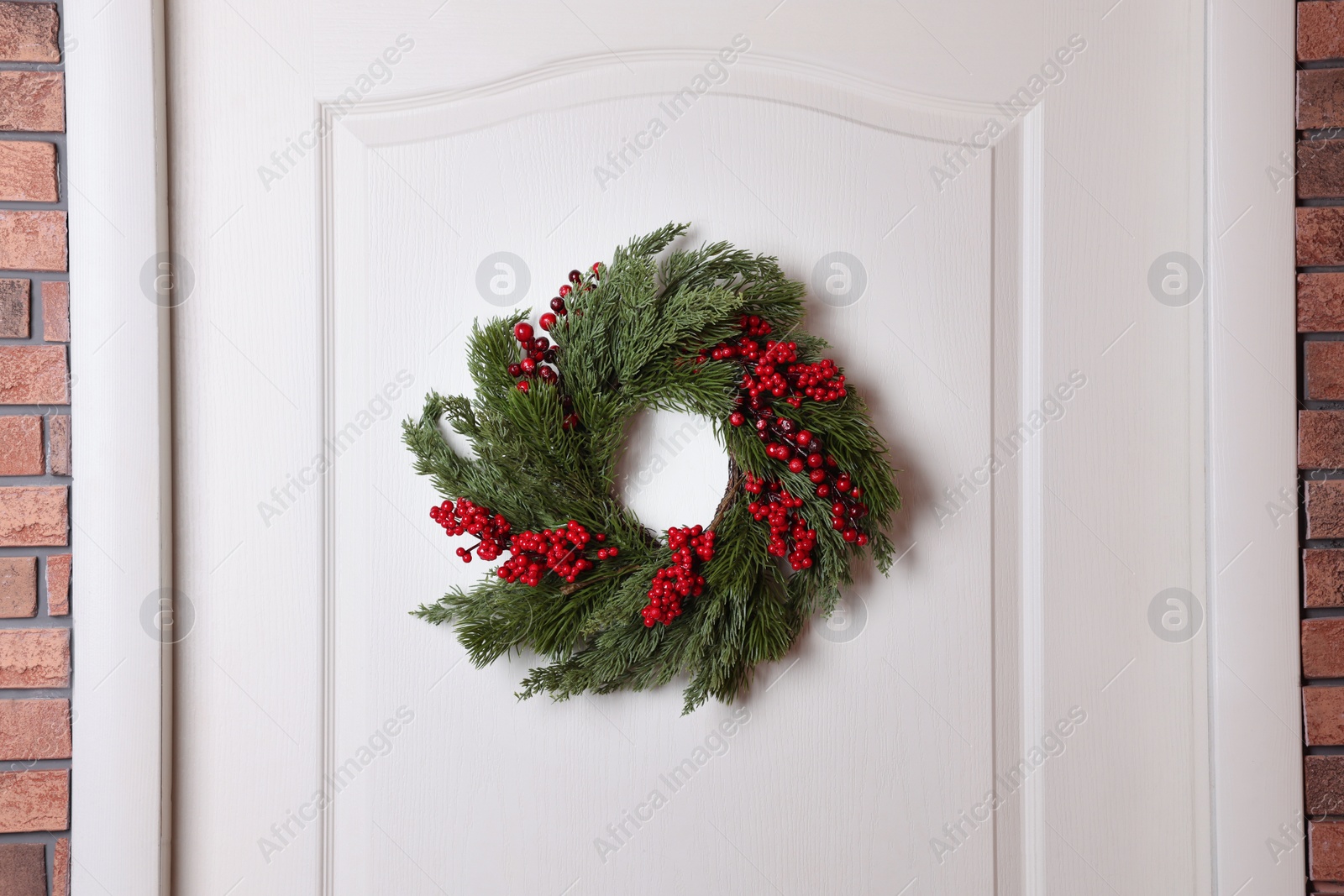 Photo of Beautiful Christmas wreath with red berries hanging on white door
