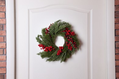 Beautiful Christmas wreath with red berries hanging on white door