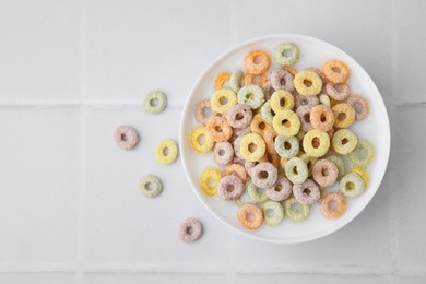 Photo of Cereal rings and milk in bowl on white tiled table, top view. Space for text