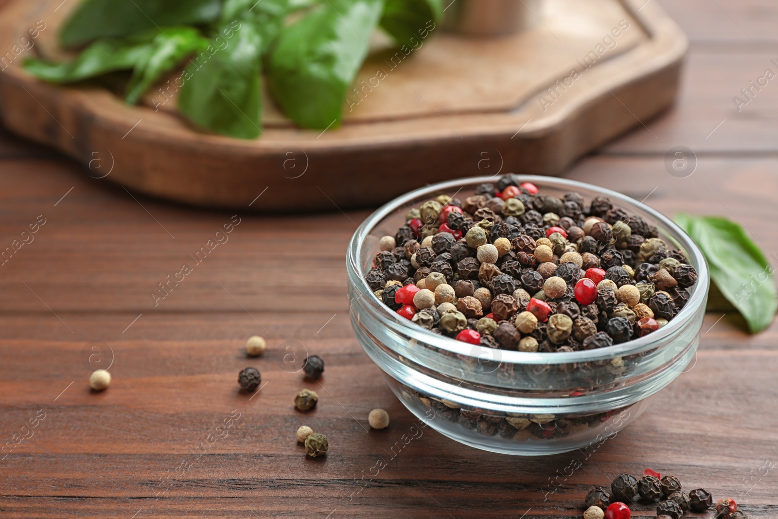 Photo of Glass bowl of mixed pepper corns on wooden table, space for text