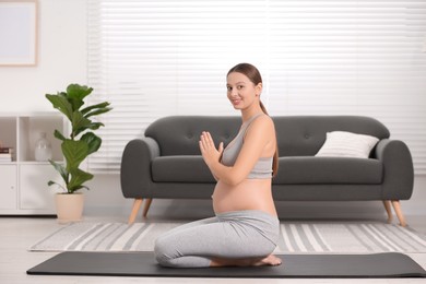 Pregnant woman meditating on yoga mat at home