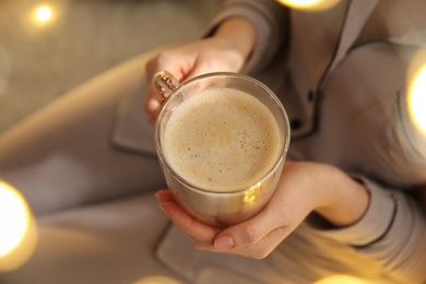 Photo of Woman holding cup with hot drink indoors, closeup