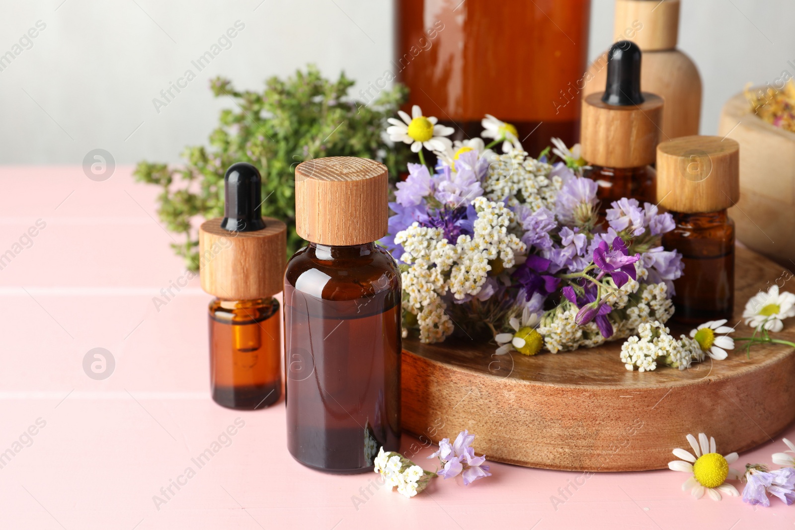 Photo of Aromatherapy. Different essential oils and flowers on pink wooden table