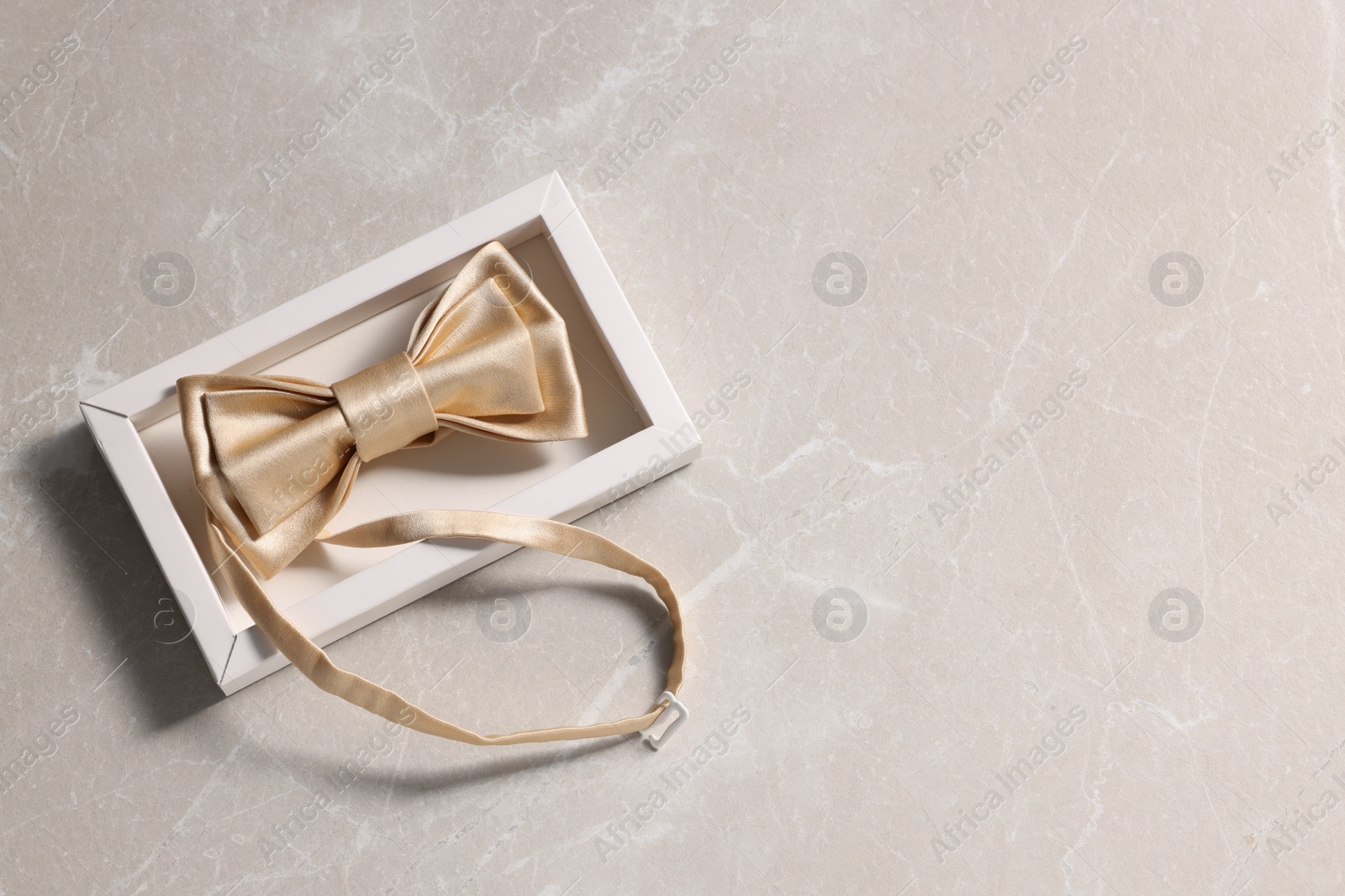 Photo of Stylish pale yellow bow tie on beige marble background, top view