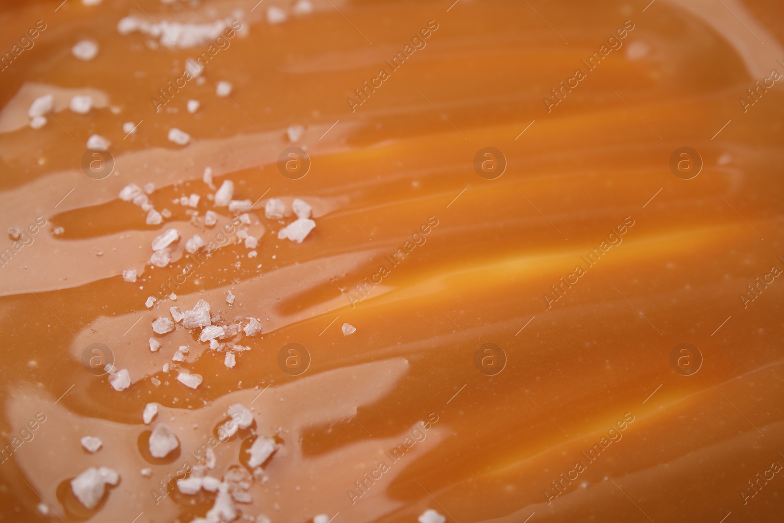 Photo of Delicious caramel sauce with sea salt as background, closeup