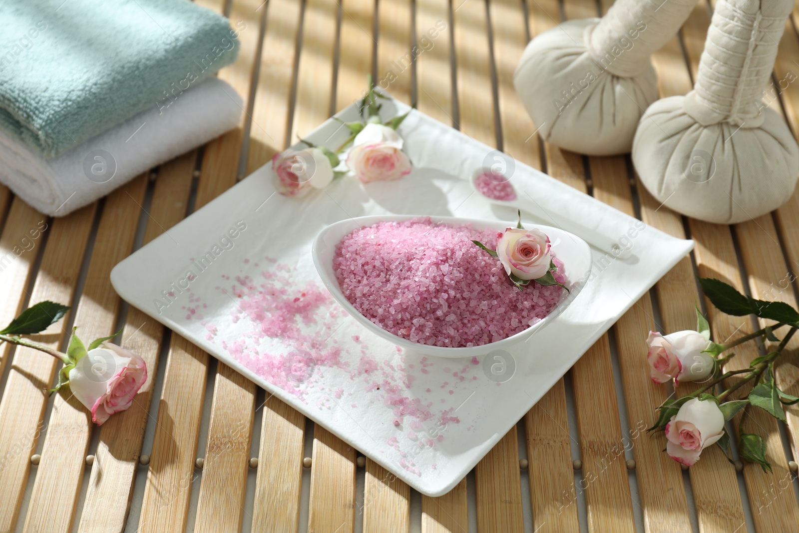 Photo of Bowl of pink sea salt and beautiful roses on wooden table