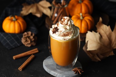 Photo of Glass of pumpkin spice latte with whipped cream and ingredients on black table