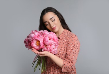 Beautiful young woman with bouquet of peonies on light grey background