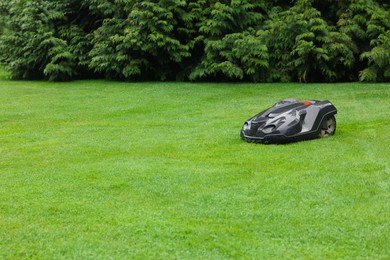 Photo of Modern lawn mower on green grass outdoors. Space for text