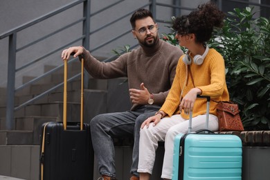 Photo of Being late. Worried couple with suitcases sitting on bench outdoors