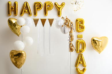 Phrase HAPPY BIRTHDAY made of golden balloon letters on white wall