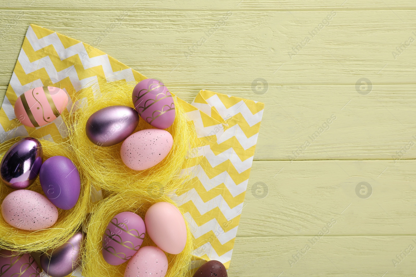 Photo of Decorative nests with many beautiful Easter eggs on yellow wooden table, flat lay. Space for text