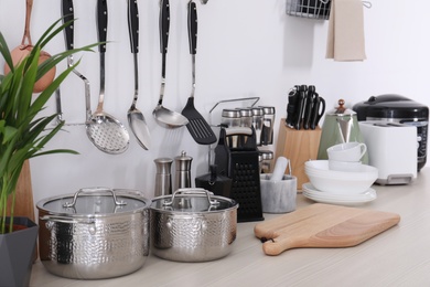 Photo of Set of clean cookware, dishes, utensils and appliances on table at white wall