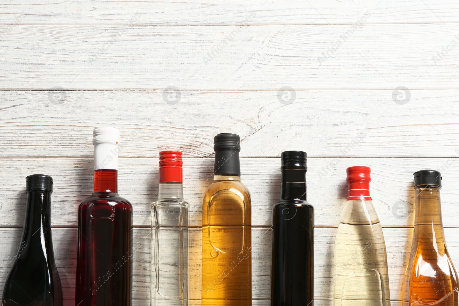 Photo of Flat lay composition with different kinds of vinegar in bottles and space for text on wooden background