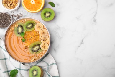 Bowl of delicious fruit smoothie with fresh banana, kiwi slices and granola on white marble table, flat lay. Space for text